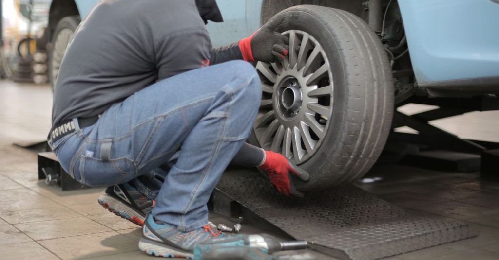 Mechanic changing a car tire indoors, using tools for vehicle maintenance.